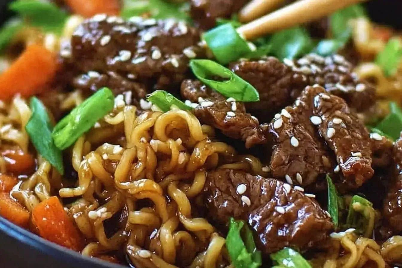 Close-up of Slow Cooker Beef Ramen Noodles with tender beef slices, green onions, and sesame seeds in a savory broth.