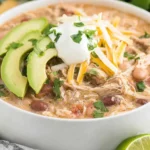 Creamy Crockpot White Chicken Chili topped with avocado slices, cheese, and sour cream in a white bowl.