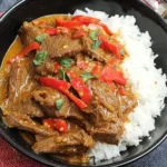 Slow Cooker Satay Beef served with white rice and red bell peppers, garnished with fresh cilantro.