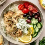 Slow Cooker Greek Chicken served with rice, cucumbers, olives, tomatoes, and tzatziki sauce in a bowl.