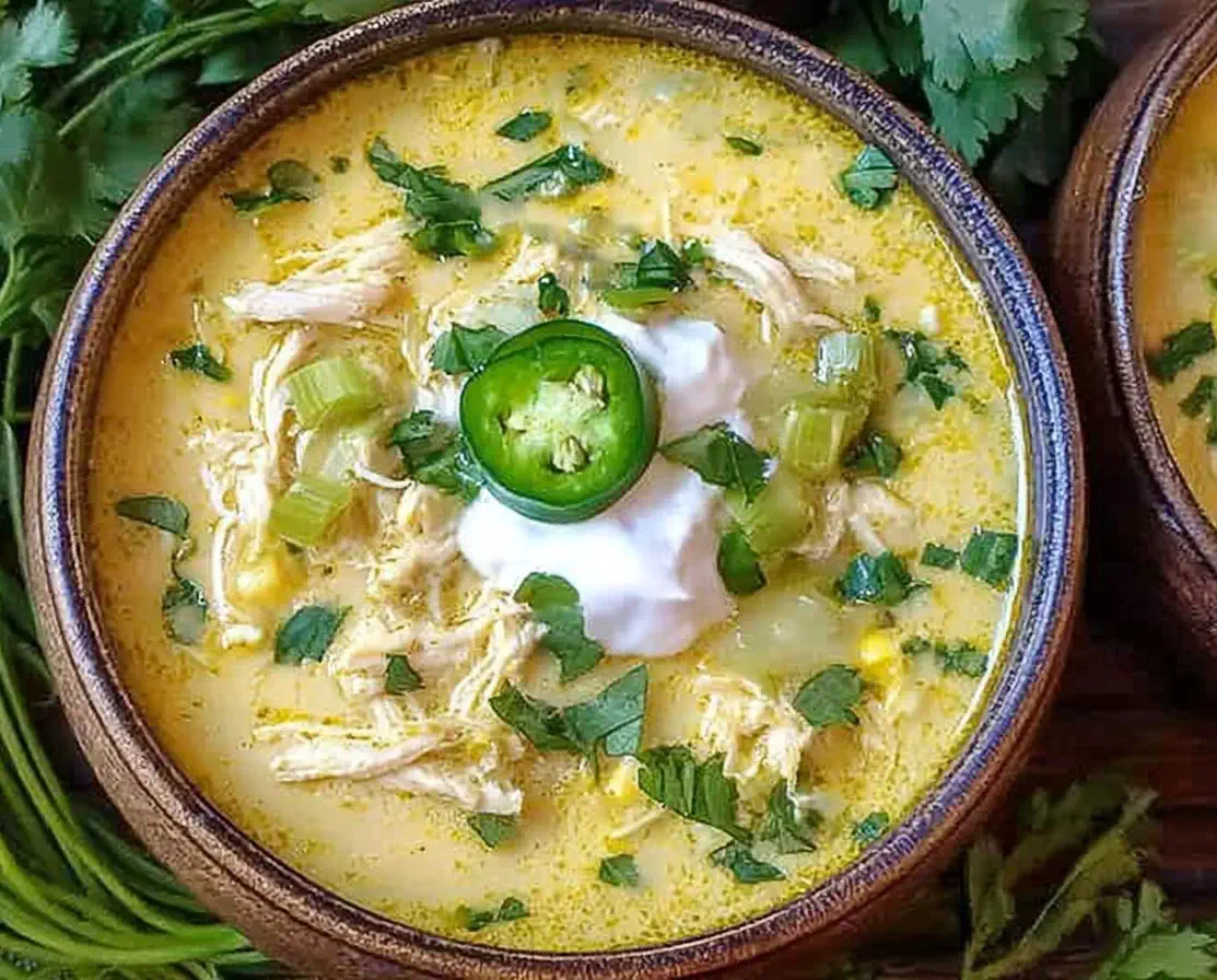 Bowl of Slow Cooker Green Enchiladas Chicken Soup topped with sour cream, jalapeño slices, and fresh cilantro for a creamy and flavorful comfort meal.