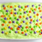 Halloween Poke Cake with colorful candy toppings and creamy green frosting.
