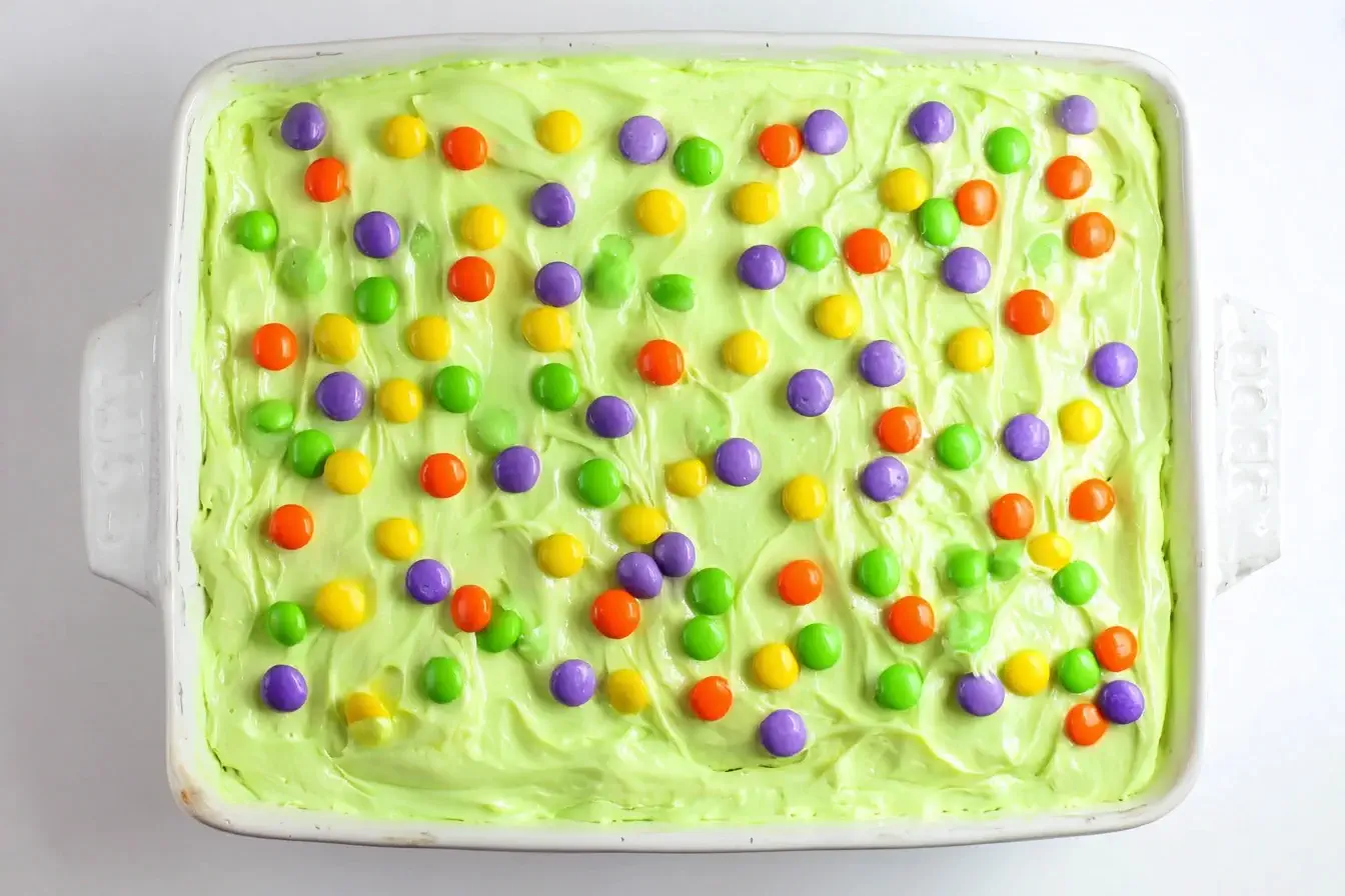 Halloween Poke Cake with colorful candy toppings and creamy green frosting.