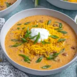 Warm bowl of Crockpot Creamy Pumpkin Chili topped with cheddar cheese, sour cream, and green onions.