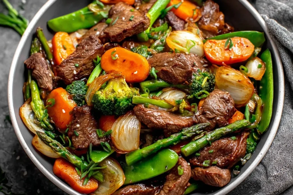 Beef Stir Fry with Vegetables bowl filled with beef strips, snap peas, carrots, broccoli, and asparagus.