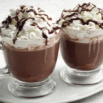 Two mugs of No-Brainer Crockpot Slow Cooker Hot Chocolate Recipe topped with whipped cream and chocolate drizzle.