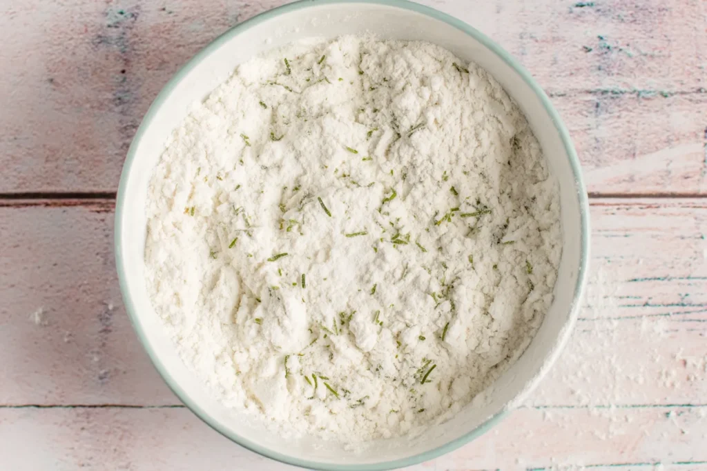 Dry ingredients for Garlic Bread Rolls including flour, herbs, sugar, and yeast combined in a bowl, ready to mix.