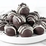 No Bake Holiday Oreo Truffles stacked on a white plate with white chocolate drizzle and crushed Oreos
