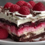 Slice of Raspberry Chocolate Lasagna Dessert topped with whipped cream, chocolate shavings, and fresh raspberries on a plate.