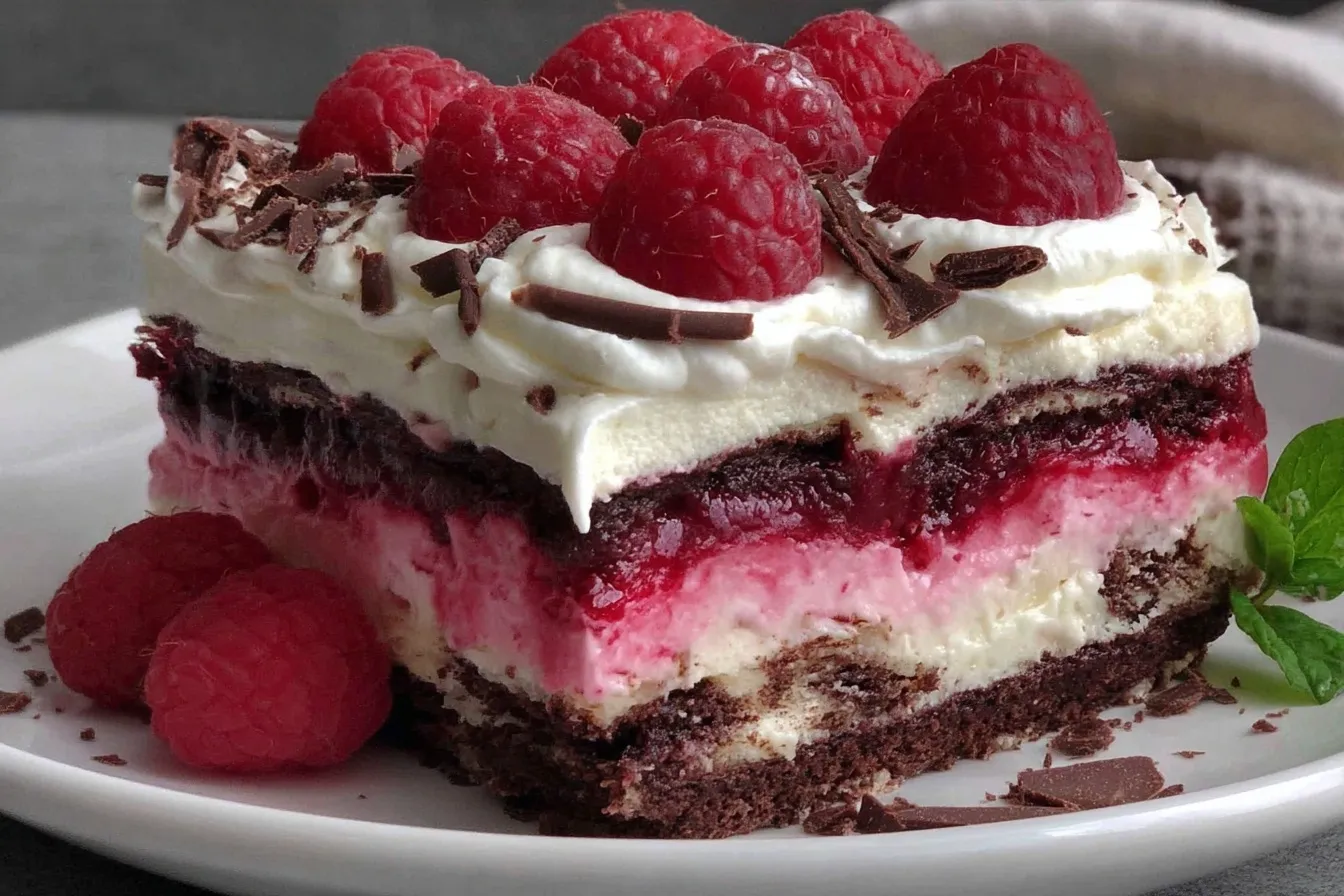 Slice of Raspberry Chocolate Lasagna Dessert topped with whipped cream, chocolate shavings, and fresh raspberries on a plate.