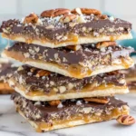 Saltine Cracker Toffee pieces layered with caramel, chocolate, and pecans, stacked in a tall pile for a holiday treat.