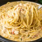 A creamy serving of CrockPot Chicken Spaghetti lifted with a fork, showing tender noodles coated in rich cheese sauce.