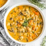 Creamy bowl of Vegan Pumpkin Wild Rice Soup with carrots, herbs, and wild rice in a white bowl.