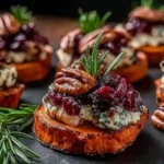 Sweet Potato Rounds with Brie Cranberry and Pecans garnished with fresh rosemary and toasted pecans on a dark serving board