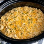 Creamy Crock Pot Chicken and Rice in a slow cooker topped with melted cheddar cheese and fresh herbs