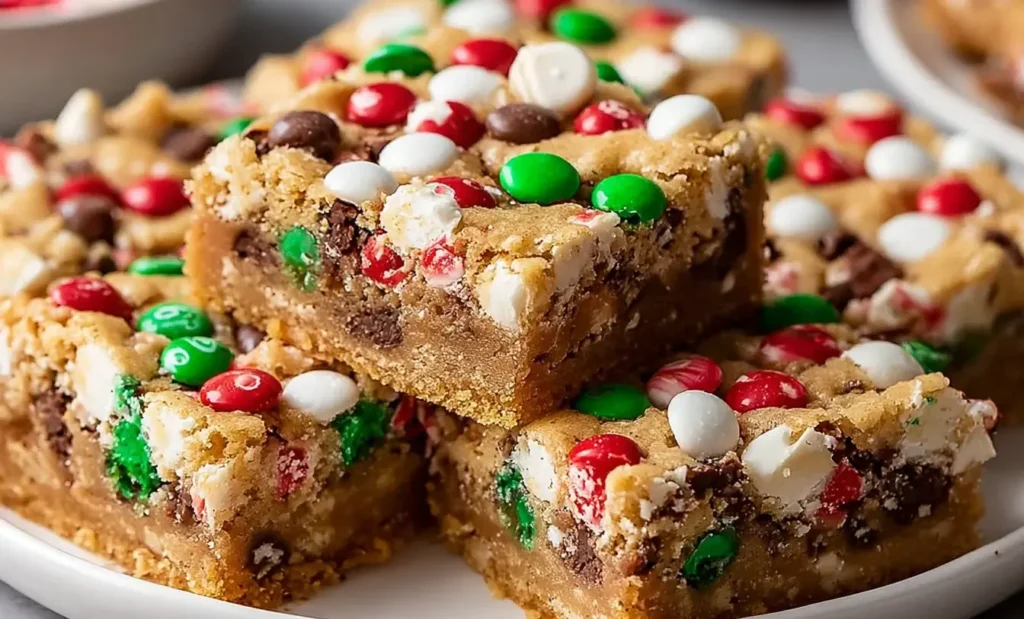 Christmas Cookie Bars stacked on a plate, filled with red, green, and white candies and chocolate chips for a festive, chewy holiday dessert.