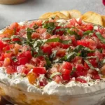 Bruschetta Dip layered with creamy cheese, fresh tomatoes, basil, and garlic served with toasted baguette slices.