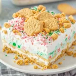 Slice of No Bake Christmas Cookie Lush topped with festive sprinkles and cookie pieces on a white plate.