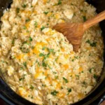 Creamy Crock Pot Chicken and Rice being stirred with a wooden spoon in a slow cooker