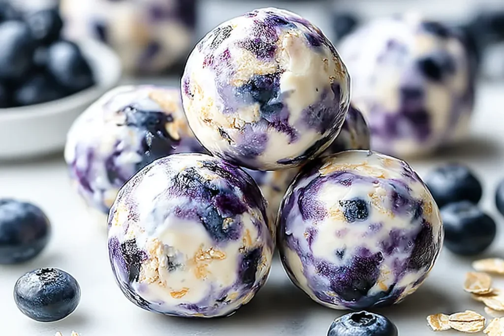 Close-up view of Blueberry Cheesecake Protein Bites stacked together, showing creamy swirls, oats, and fresh blueberries.
