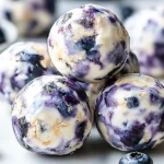 Close-up view of Blueberry Cheesecake Protein Bites stacked together, showing creamy swirls, oats, and fresh blueberries.