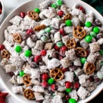 Festive bowl of Reindeer Food Recipe (Christmas Puppy Chow) with Chex cereal, pretzels, red and green M&Ms, and powdered sugar — a sweet holiday snack mix.