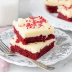 Red Velvet Cookie Bars topped with creamy frosting stacked on a decorative plate.
