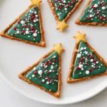 Pretzel and Candy Melt Christmas Trees arranged on a white plate, featuring pretzel triangle frames filled with green candy melts and festive sprinkles.