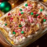Christmas Cookie Lasagna topped with whipped cream, crushed cookies, peppermint candies, and festive sprinkles in a glass dish.