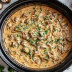 Creamy Crockpot Beef Stroganoff with tender beef, mushrooms, and rich sour cream sauce topped with fresh parsley in a slow cooker.