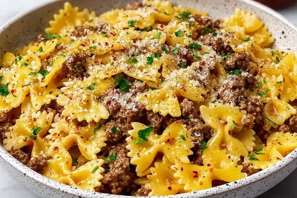 Garlic Butter Bowtie Pasta with Ground Beef sprinkled with Parmesan, parsley, and red pepper flakes in a ceramic bowl.