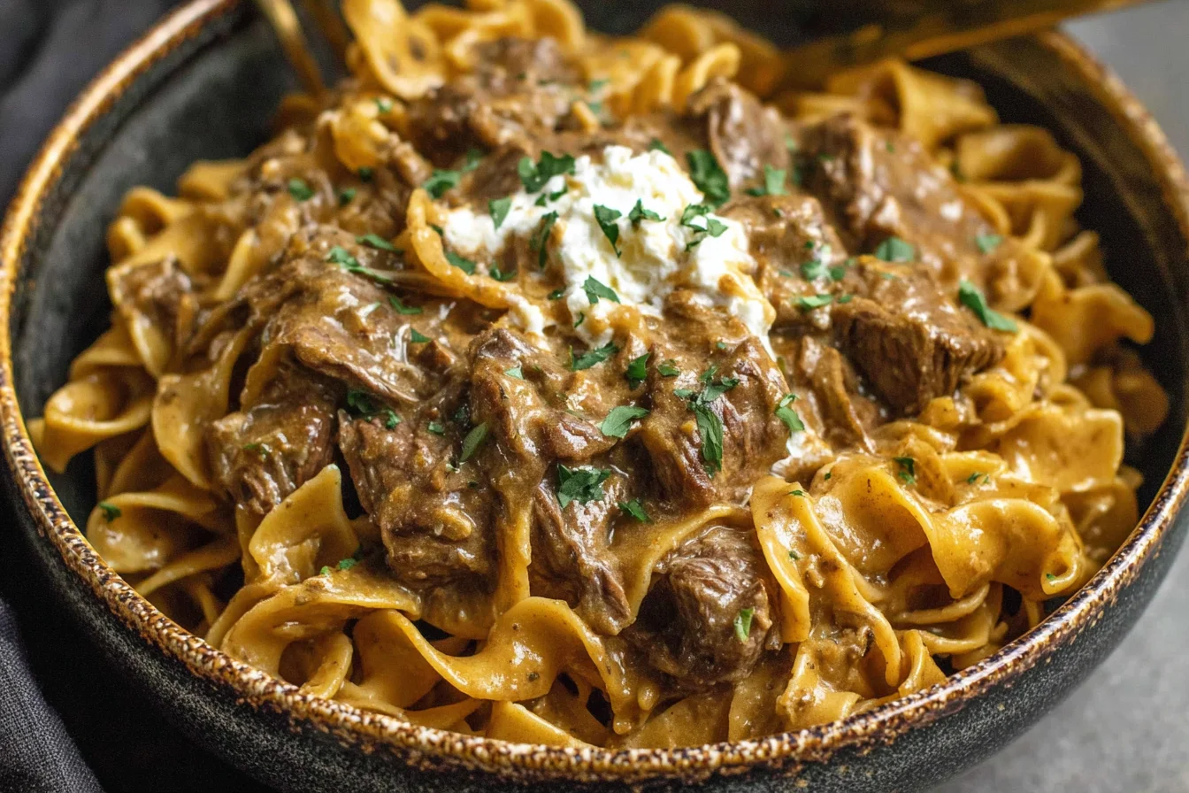 Crock Pot French Onion Beef And Noodles served over egg noodles with creamy sauce and fresh parsley on top