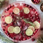 Festive Non Alcoholic Christmas Punch with cranberries, lime slices, rosemary, and ice in a glass bowl for holiday celebrations.