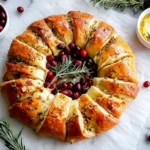 Cranberry Brie Crescent Wreath served on parchment paper with fresh cranberries and rosemary in the center.