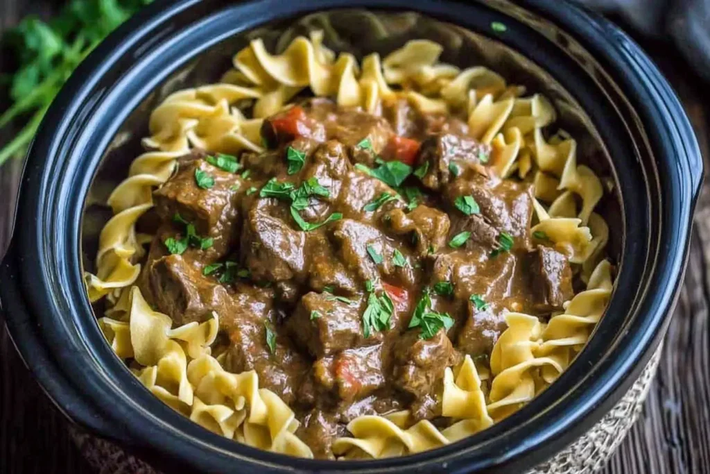Slow Cooker Beef and Noodles in a crockpot with tender beef chunks and egg noodles topped with fresh herbs