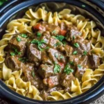 Slow Cooker Beef and Noodles in a crockpot with tender beef chunks and egg noodles topped with fresh herbs