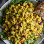 Best Curried Chickpea Salad served over greens with bread slices and colorful veggies.