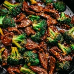 Chinese Beef And BroccoliChinese Beef and Broccoli simmering in a savory sauce inside a cast-iron skillet.