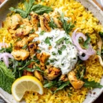 Dump-and-Bake Chicken Tzatziki with Rice served in a bowl with golden rice, seasoned chicken, creamy tzatziki, fresh herbs, and lemon