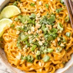 Creamy Gluten Free Red Curry Peanut Noodles topped with cilantro, peanuts, and lime wedges in a white bowl