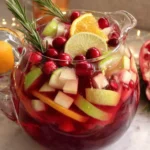 Non-Alcoholic Christmas Sangria in a glass pitcher with apples, citrus slices, cranberries, and rosemary