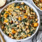 A bowl of One Pot Fall Vegetable Orzos with chickpeas, kale, and butternut squash topped with Parmesan.