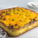 Overnight Cheesy Sausage and Hashbrown Breakfast Casserole baked in a glass dish topped with melted cheddar and green onions.