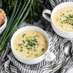 Creamy Slow Cooker Potato Leek Soup served in white bowls topped with chives beside fresh bread and green onions.