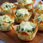 Spinach-Artichoke Dip Wonton Cups freshly baked with golden crispy edges on a wooden board.