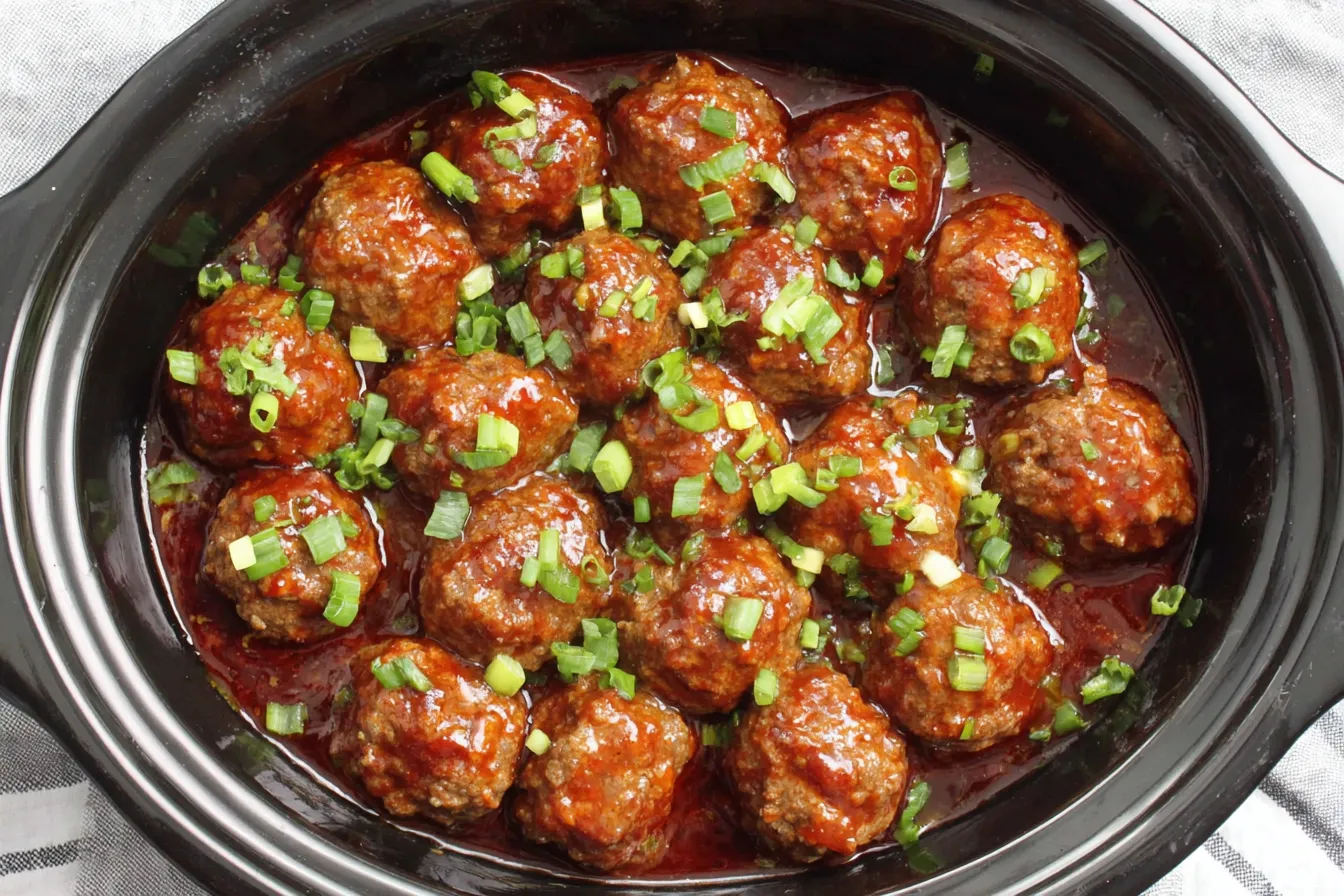 Sweet and Spicy Slow Cooker Meatballs cooking in the crockpot with a thick, flavorful sauce