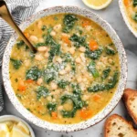Tuscan White Bean Soup in a speckled bowl with kale, carrots, and cannellini beans, garnished with Parmesan.