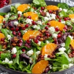 Colorful Winter Salad Recipe topped with mandarin orange slices, pomegranate seeds, feta cheese, and candied pecans on fresh greens.
