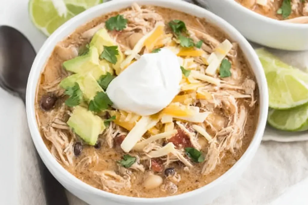 Bowl of Crockpot White Chicken Chili topped with avocado, cheese, cilantro, and sour cream.