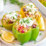 Greek Chicken Stuffed Peppers topped with feta and fresh dill, served with lemon wedges on a white plate.